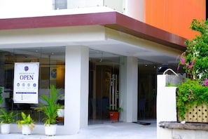 A hotel entrance with a sign indicating it's open, glass doors, potted plants, and a modern building facade.