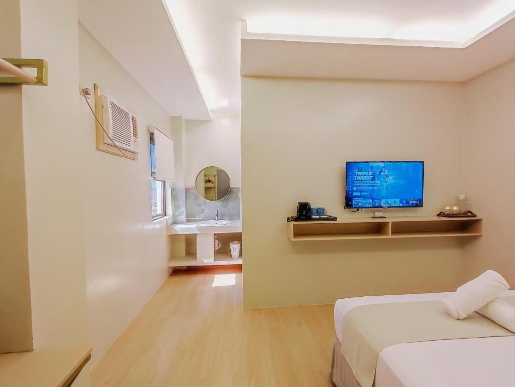 A hotel room with a bed, a television, a small shelf, and a bathroom with a mirror and sink.