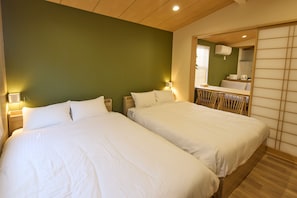 Une chambre d’hôtel avec deux lits, un plafond en bois, un mur vert et un miroir qui reflète la salle de bain.