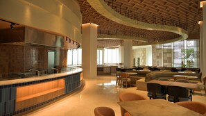 A modern hotel lobby with a curved bar, seating areas, and a high ceiling with wooden beams.