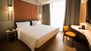 A hotel room with a large bed, bedside table, chair, desk, and a mirror.