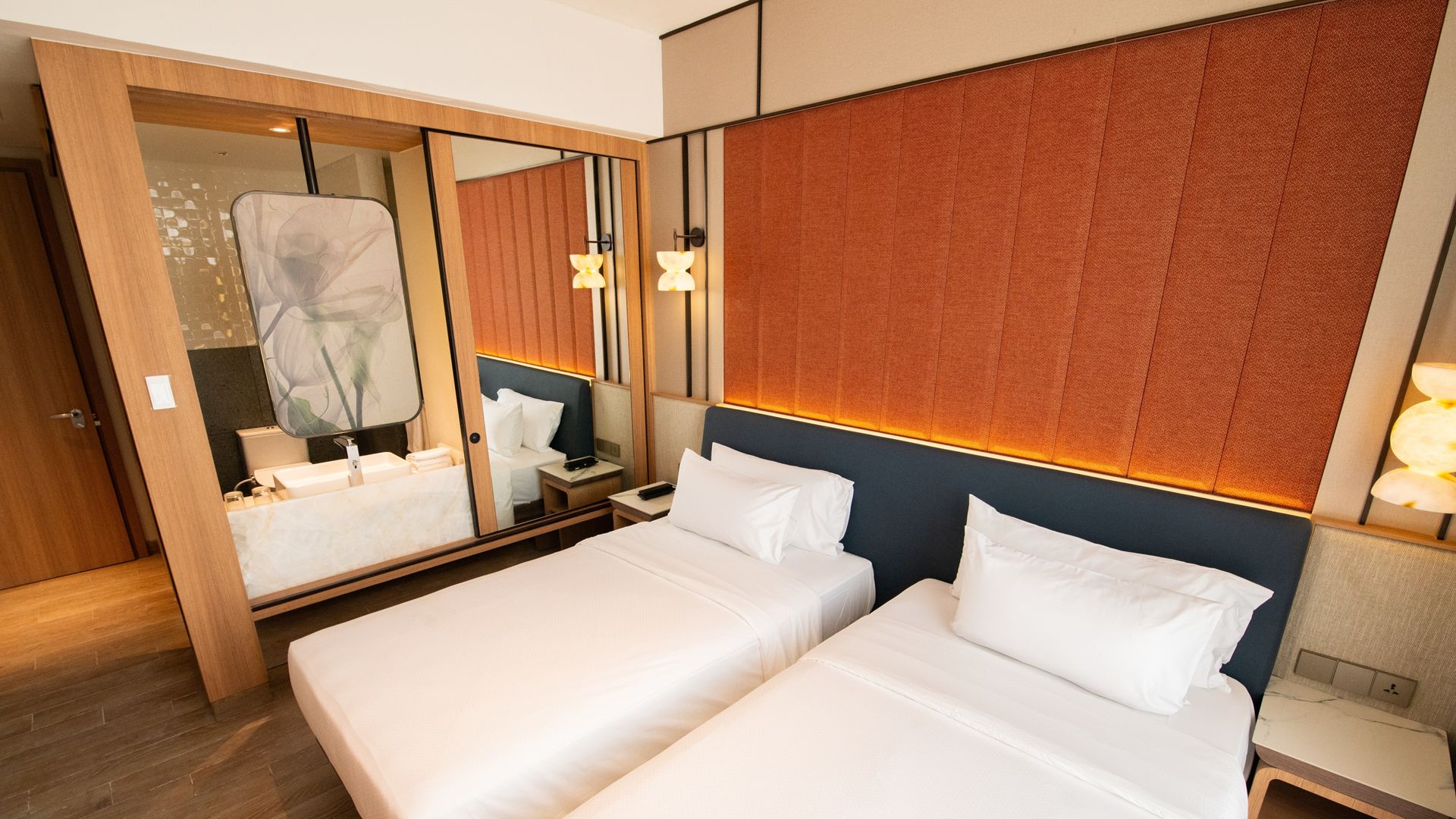 Een hotelkamer met twee bedden, een grote spiegel, een houten garderobe en een wandlamp.