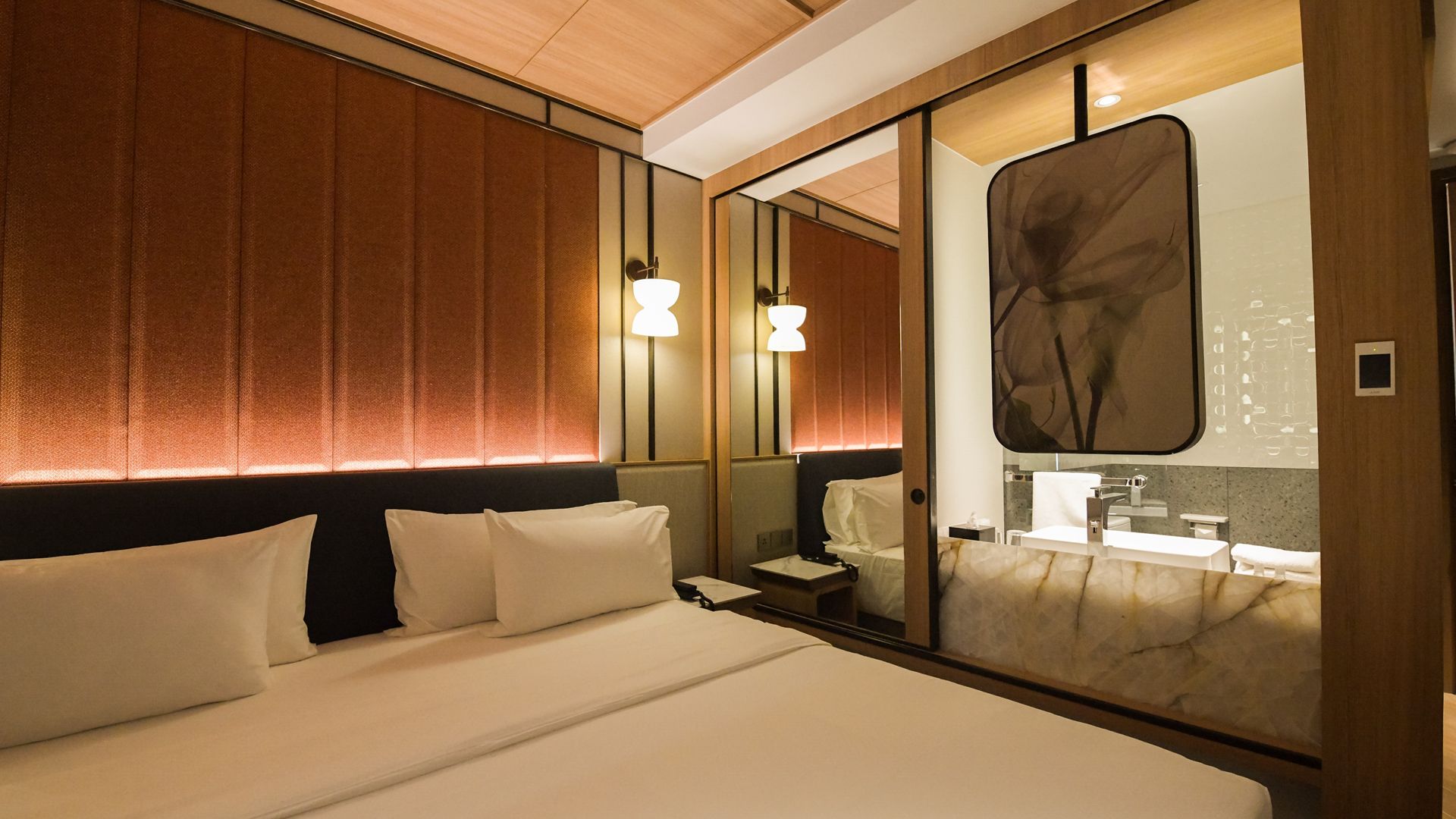 Una habitación de hotel con cama, mesita de noche, espejo y baño con lavamanos y espejo.