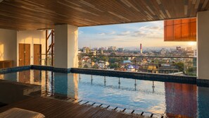 Una piscina infinita en la azotea con vista a la ciudad, terraza de madera y balaustrada de vidrio.