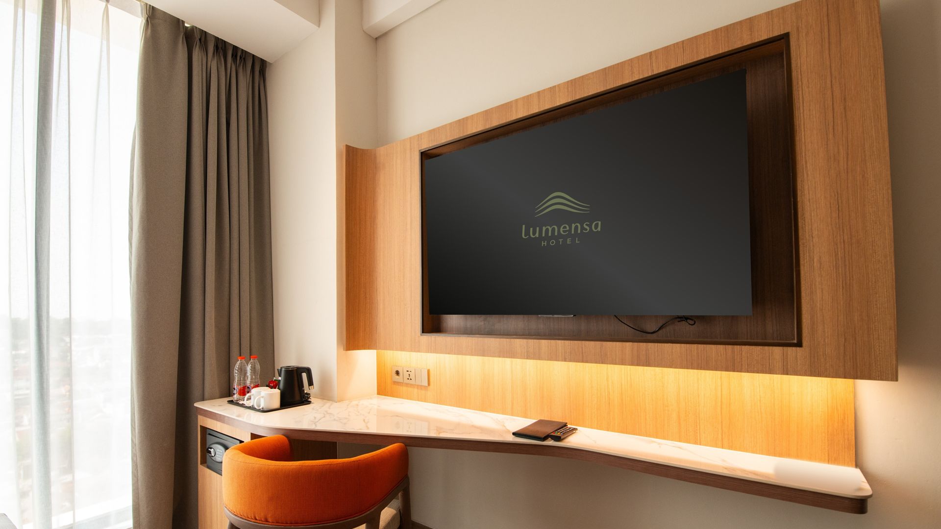 Habitación de hotel con televisor de pantalla plana montado en una pared de madera, un escritorio pequeño con una silla y una ventana con cortinas.