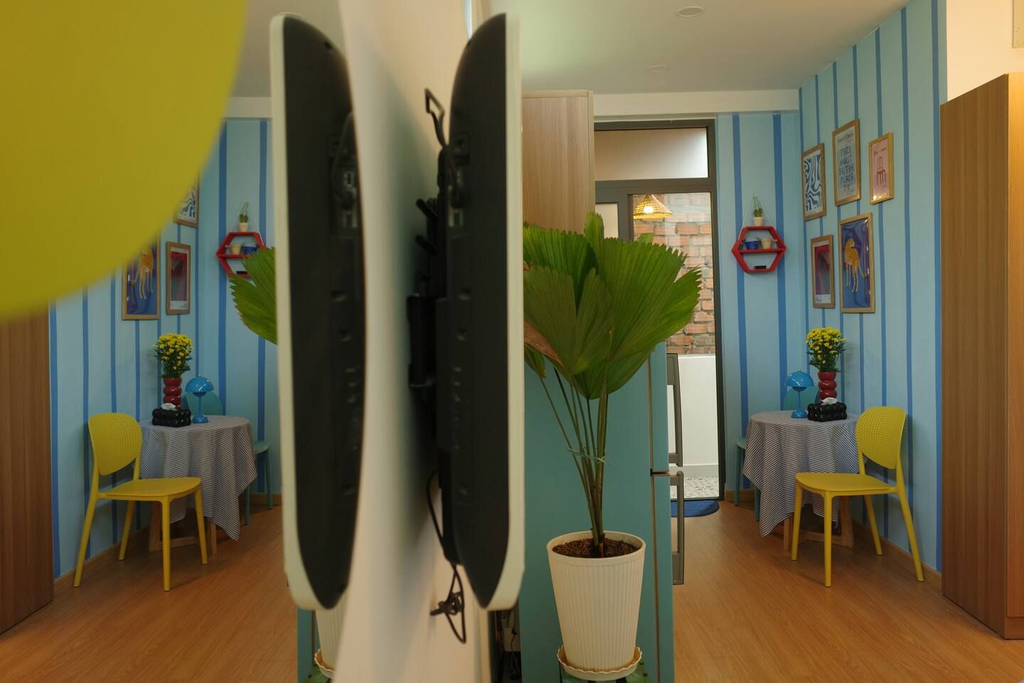 A room with a wooden floor, two yellow chairs, a table with a striped tablecloth, and a potted plant.