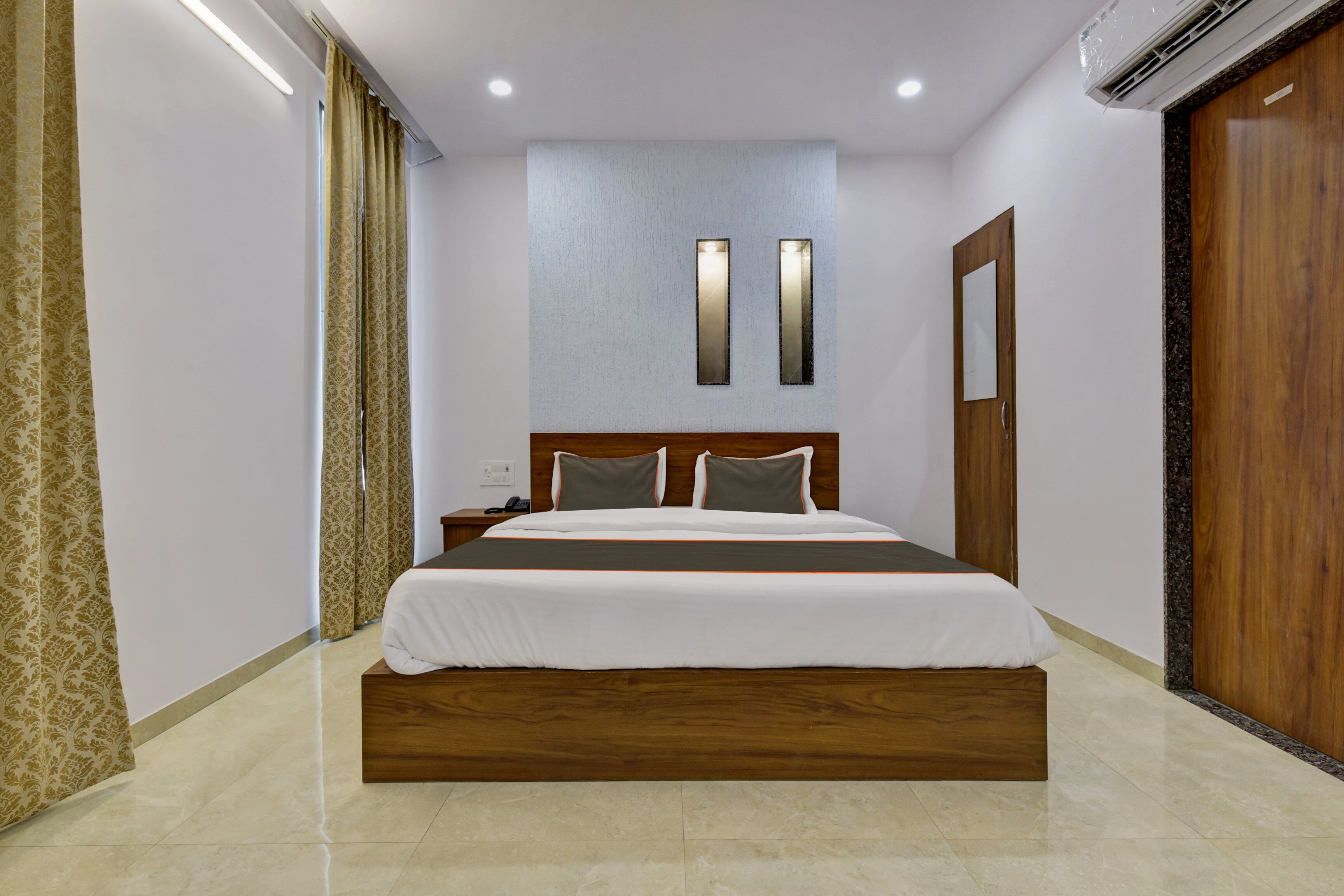 Una habitación de hotel moderna con una cama grande, cabecera de madera, mesita de noche, teléfono y armario.
