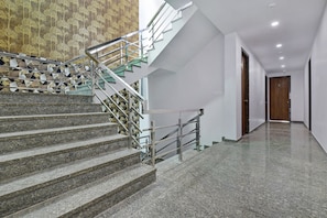 A staircase with a geometric patterned wall, a modern metal railing, and a polished stone floor leading to a hallway with a wooden door. - Hotel O Salasar Inn (Jaipur)