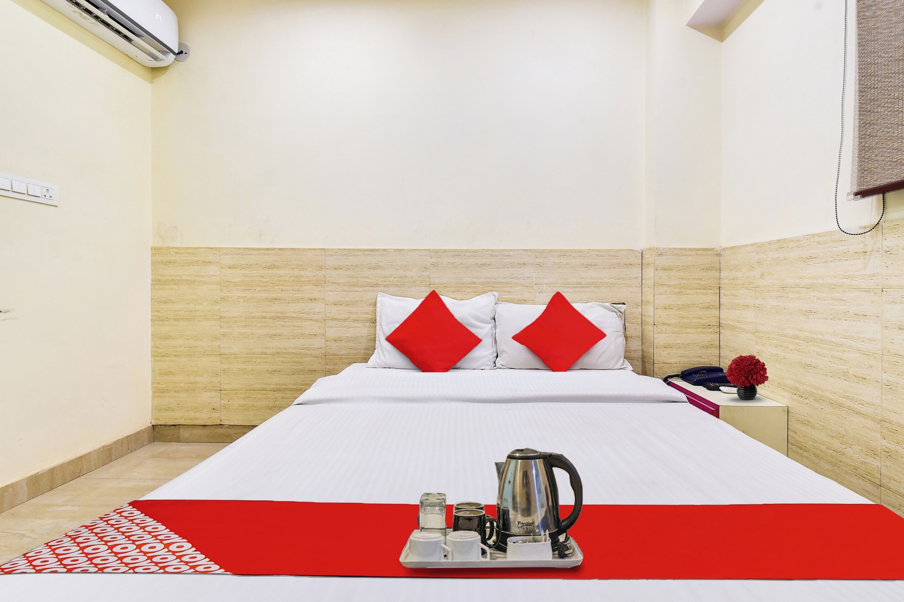 Una habitación de hotel con una cama, una mesita con tetera, tazas y un jarrón de flores.