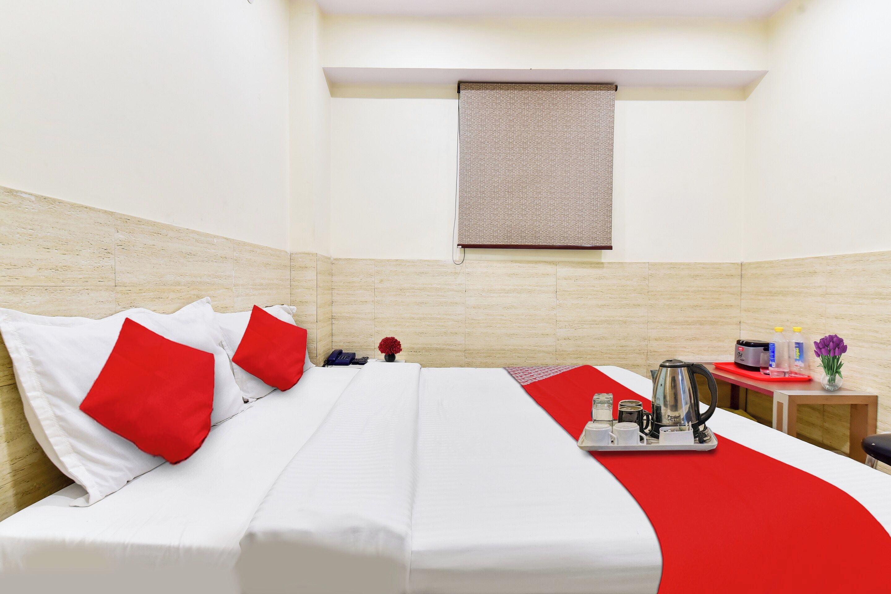 Una habitación de hotel con cama, una mesita con tetera y una ventana con persiana.