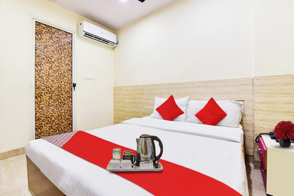 A hotel room with a bed, a tray with a kettle, and a red and white bedspread.