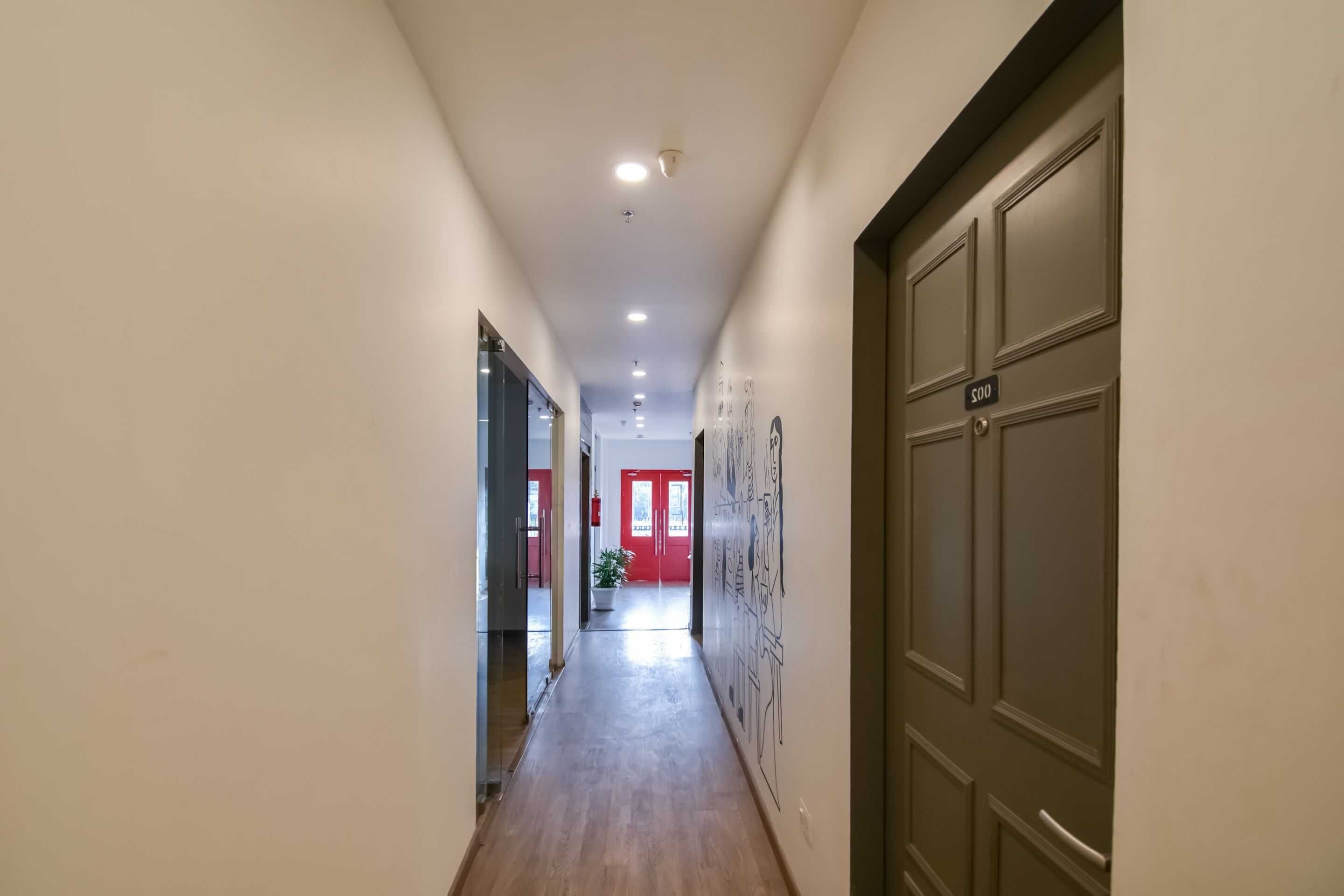A hallway with a wooden floor, a glass door on the left, and a door with a number plate on the right.