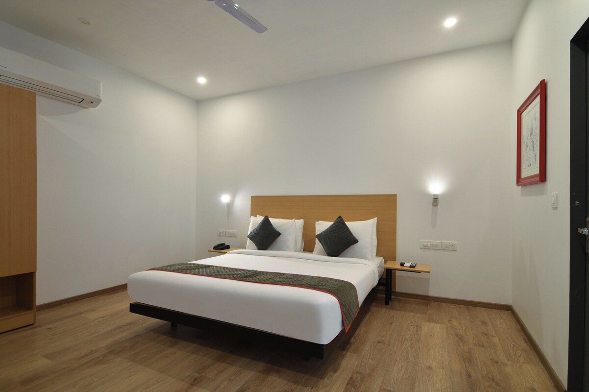 A hotel room with a bed, bedside tables, a nightstand, a wall-mounted light, and a door.
