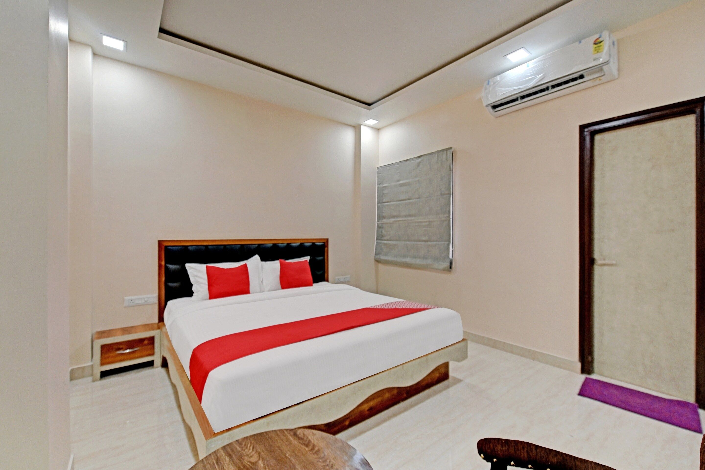 A hotel room with a bed, a bedside table, a chair, a wardrobe, and an air conditioning unit.