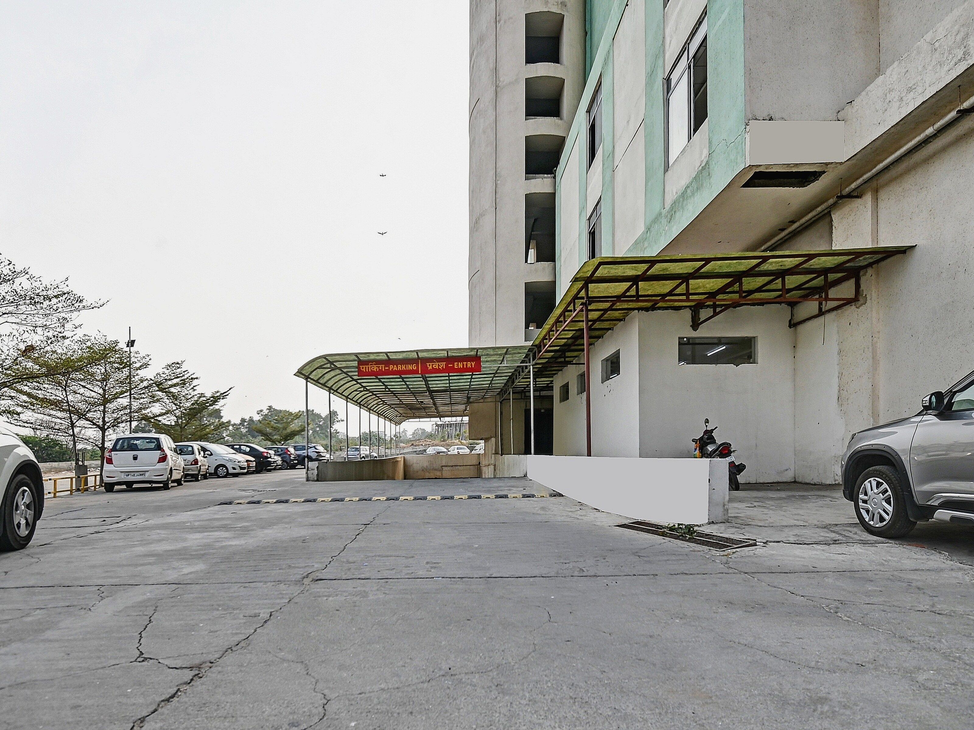 A parking area with a covered entrance, a building with multiple floors, and parked cars.