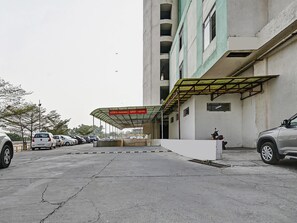 Een parkeerplaats met overdekte ingang, een gebouw met meerdere verdiepingen en geparkeerde auto's.