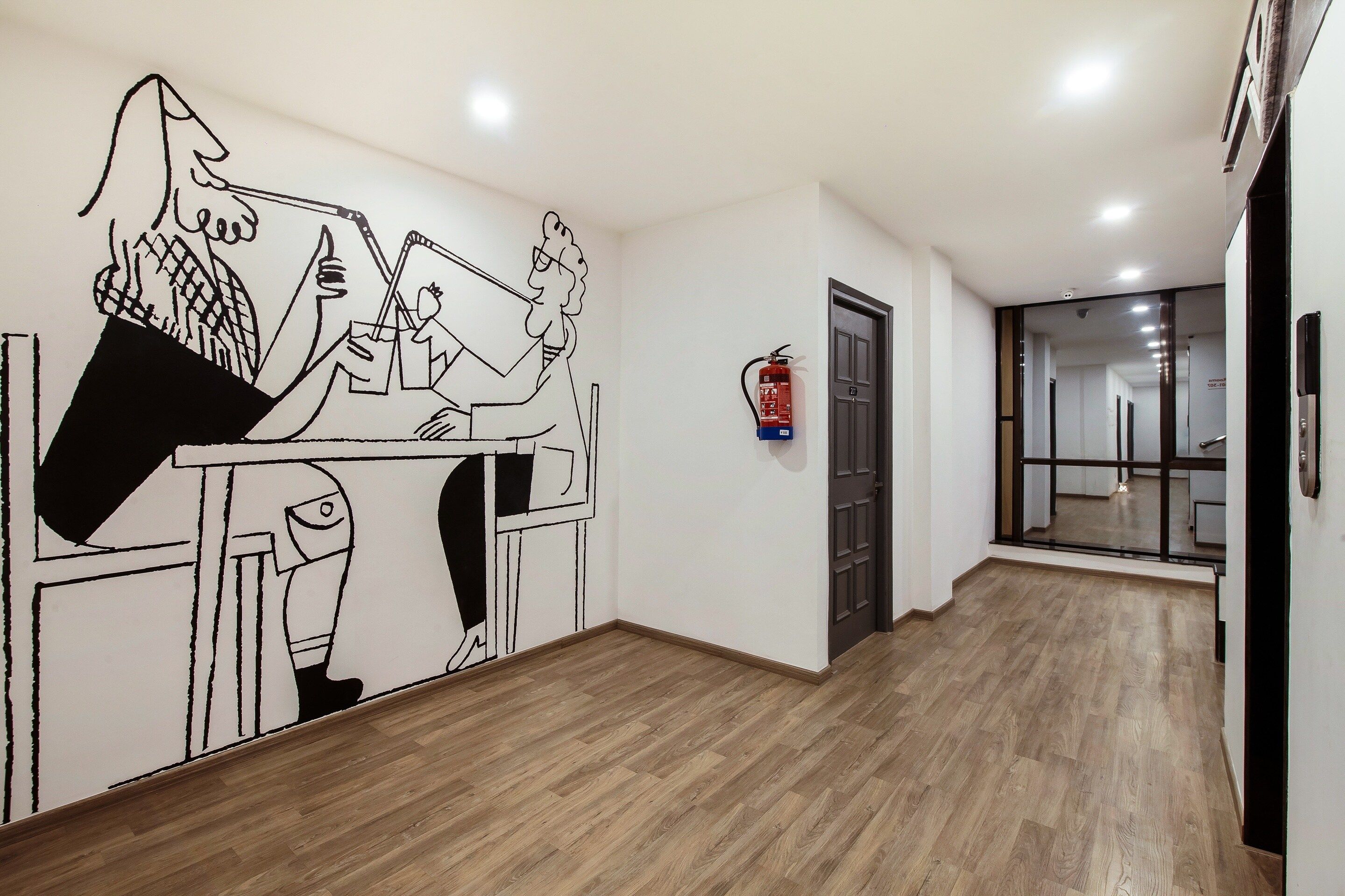 A hallway with a wooden floor, a fire extinguisher mounted on the wall, and a door at the end.