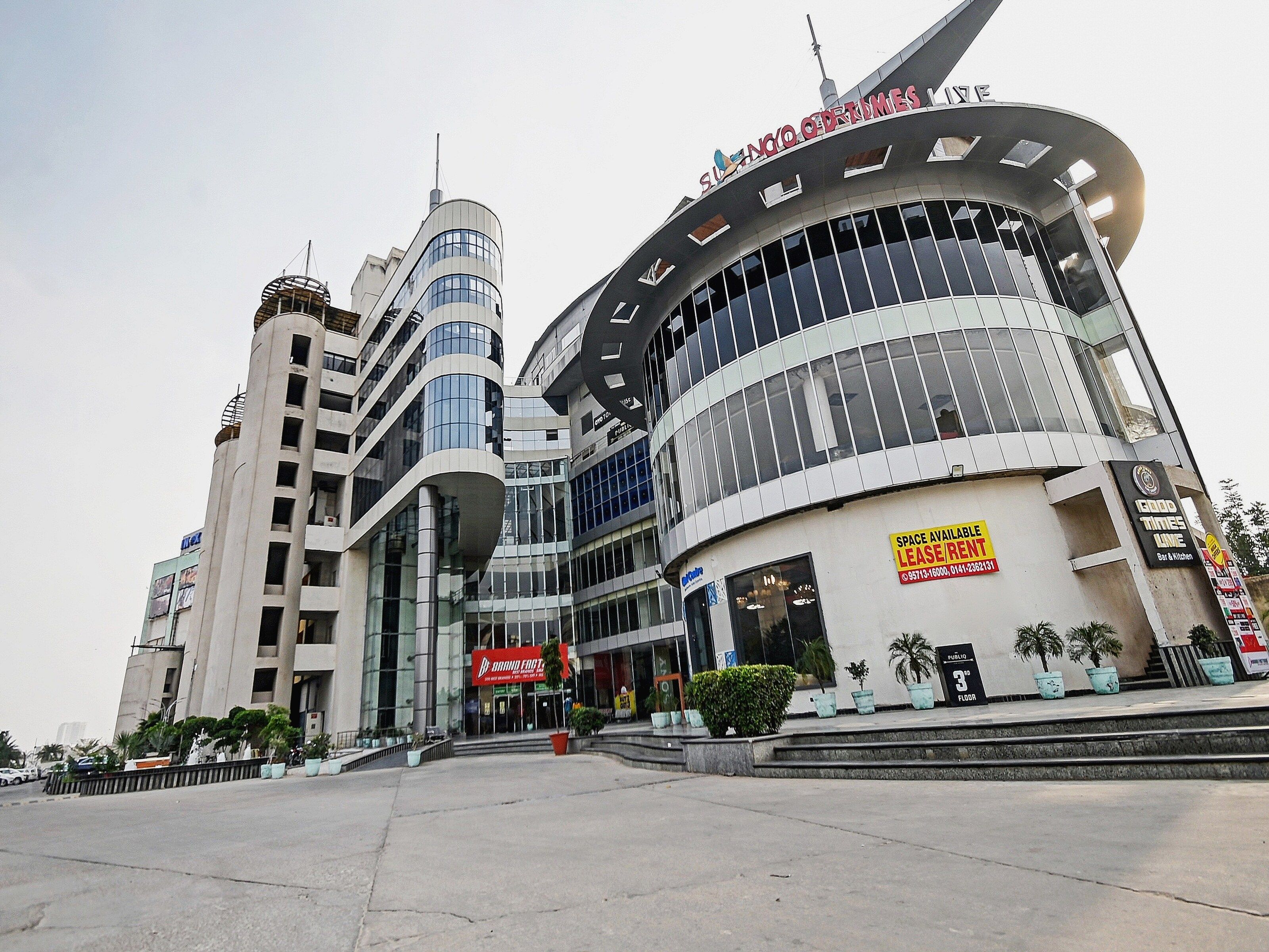 A modern building with a curved facade, a prominent clock, and a sign indicating space availability for lease.