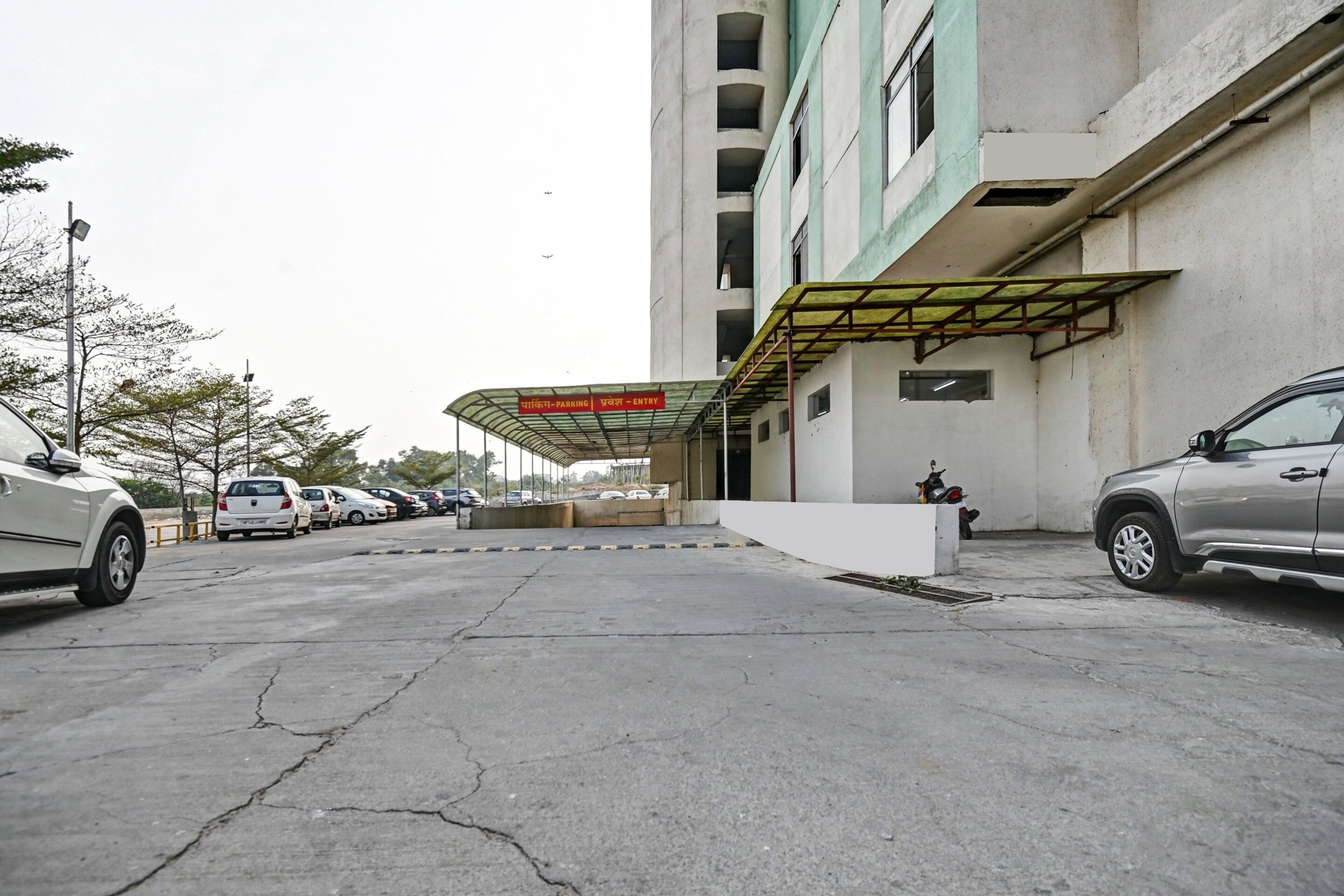 A parking area with a covered entrance, a building with multiple floors, and several parked cars.