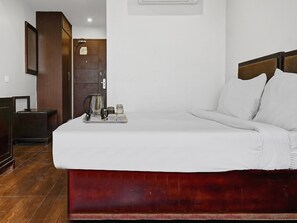Een hotelkamer met een bed, nachtkastje, houten kledingkast en een dienblad met waterkoker en kopjes.
