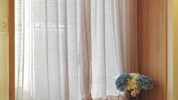 Una ventana con cortinas translúcidas y un florero sobre un alféizar de madera.