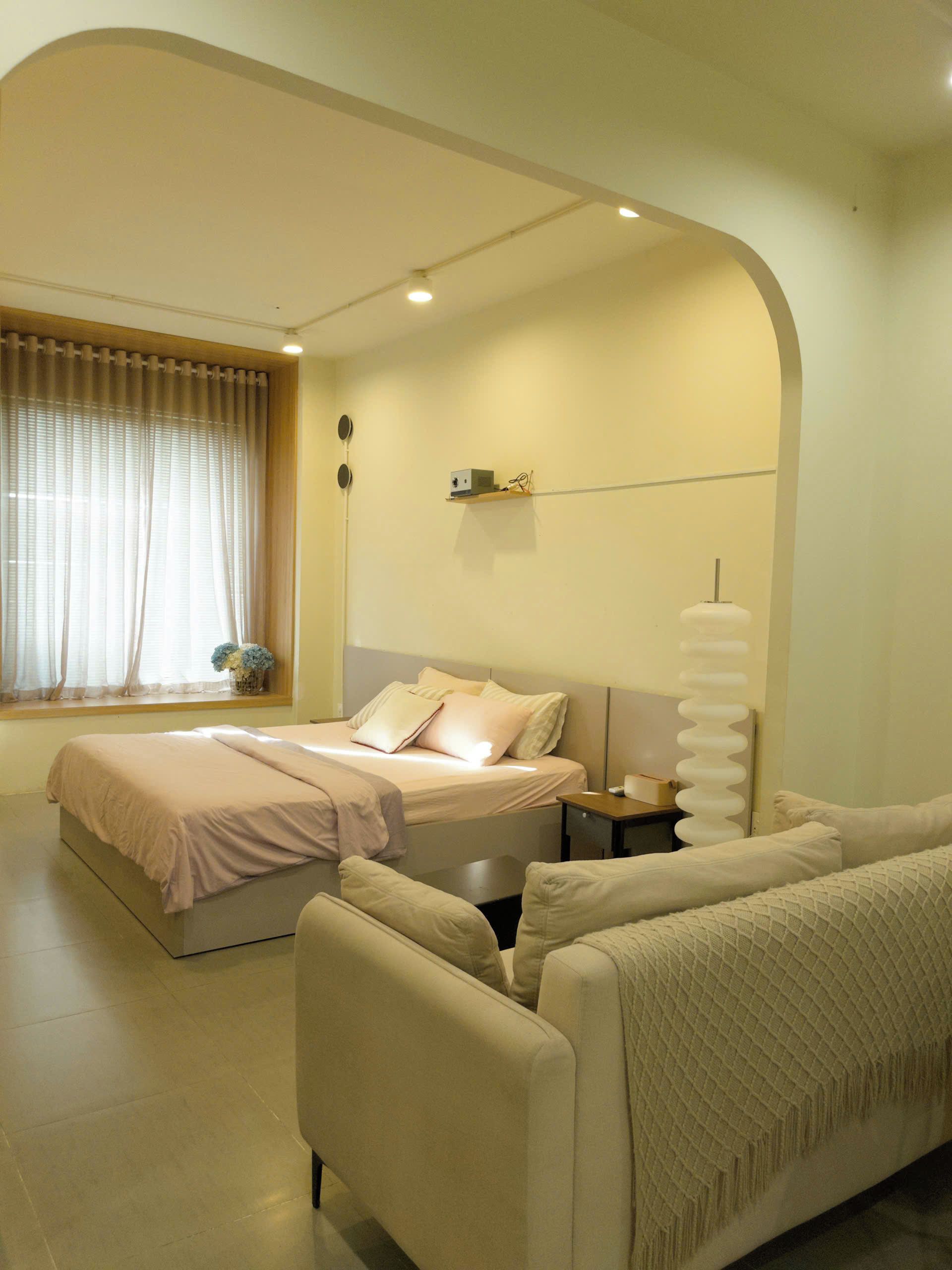 Un dormitorio con dos camas, un sofá, una mesita de noche, una lámpara y una ventana con cortinas.