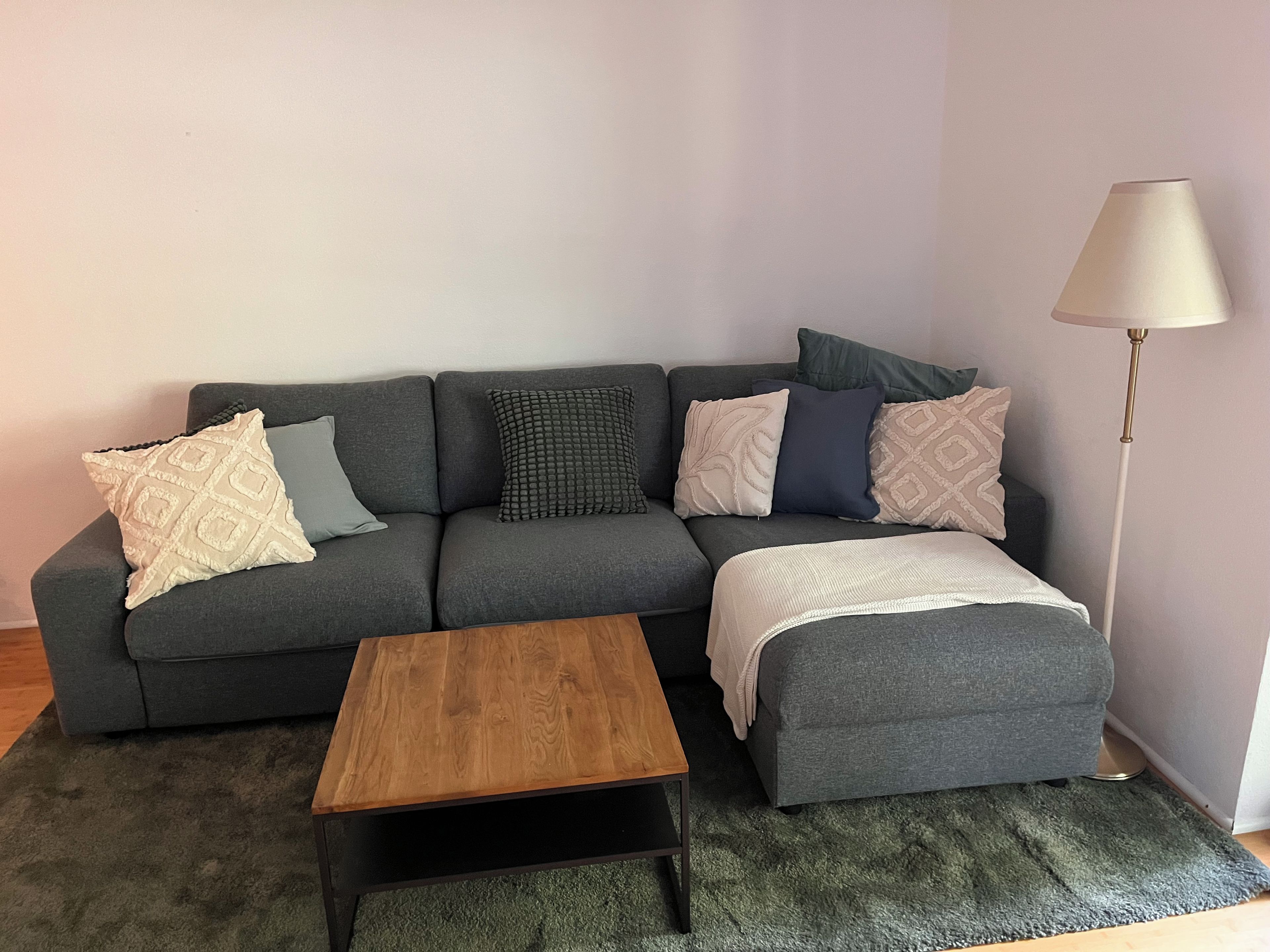 A grey sofa with patterned cushions, a wooden coffee table, and a floor lamp.