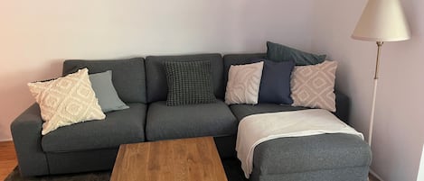 A grey sofa with patterned cushions, a wooden coffee table, and a floor lamp.