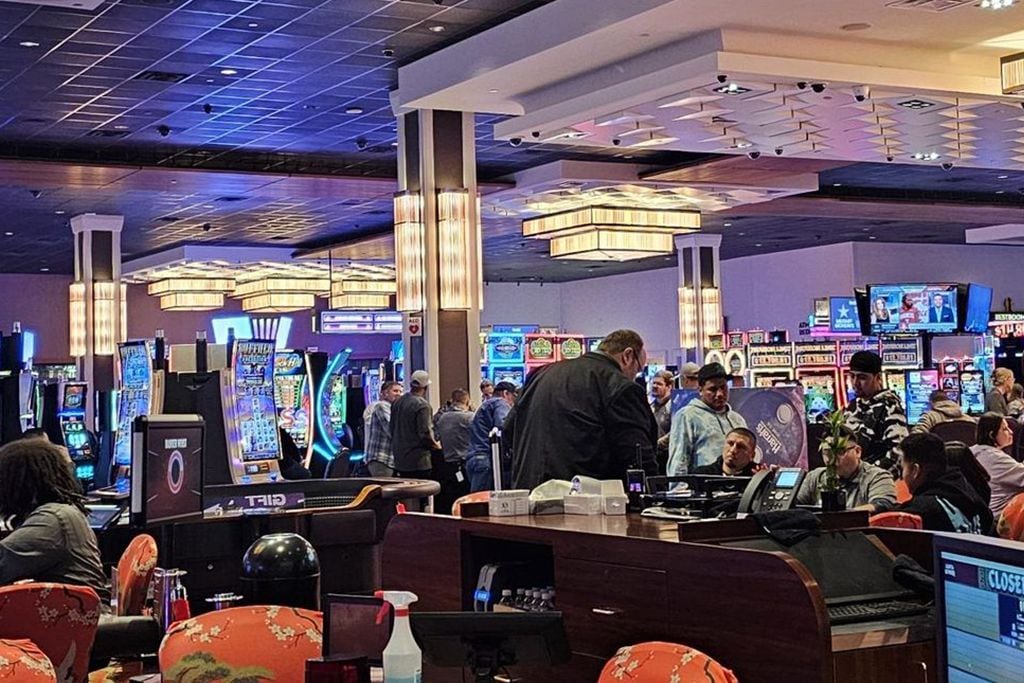Un casino avec des machines à sous, une table de blackjack et une foule de personnes.