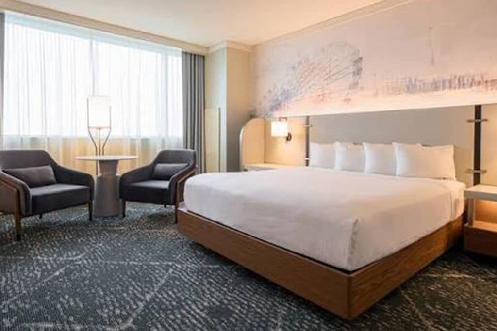 Une chambre d’hôtel avec un grand lit, deux fauteuils, une petite table et une lampe fixée au mur.