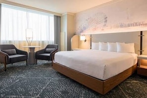 A hotel room with a large bed, two armchairs, a small table, and a wall-mounted lamp. - 1-bedroom Strip Hotel in Vegas- #1 Deal /Free Parking/No Resort Fees (Las Vegas)
