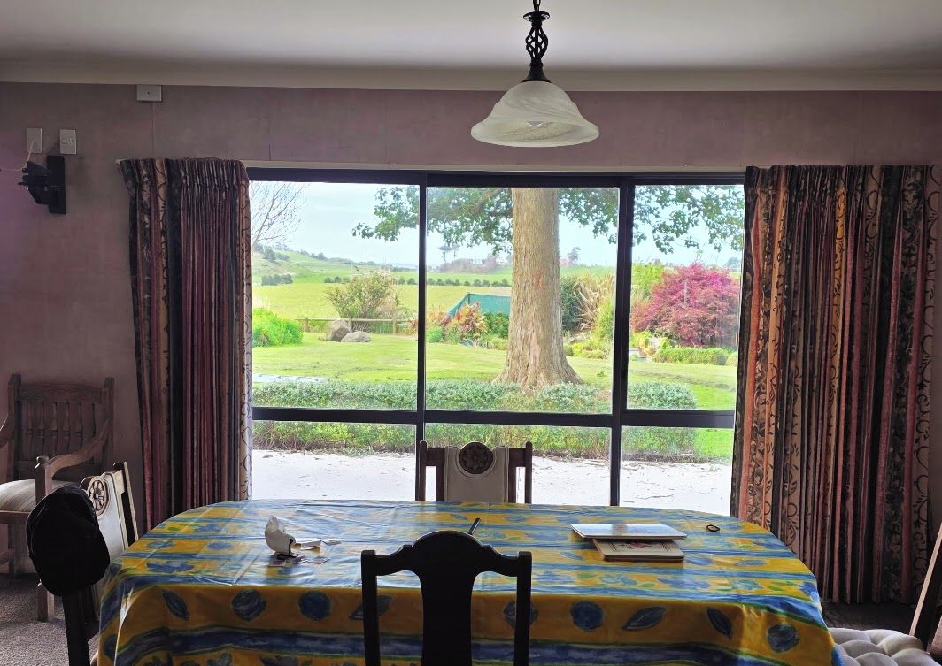 A room with a large window, a table with a tablecloth, a chair, and a hanging light fixture.