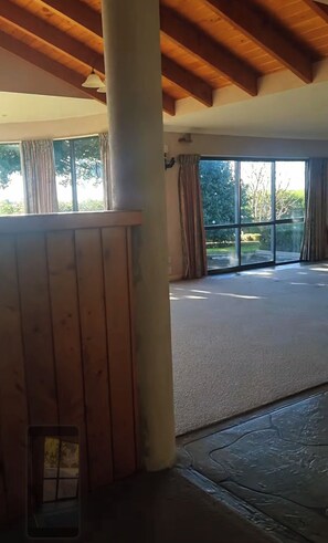 Ein Zimmer mit einer großen Schiebeglastür, die auf einen Balkon führt, Holzbalken an der Decke und Blick ins Grüne.