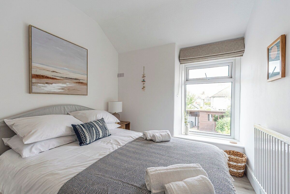 A bedroom with a large bed, a window with a view, a bedside table, and a wall-mounted artwork.