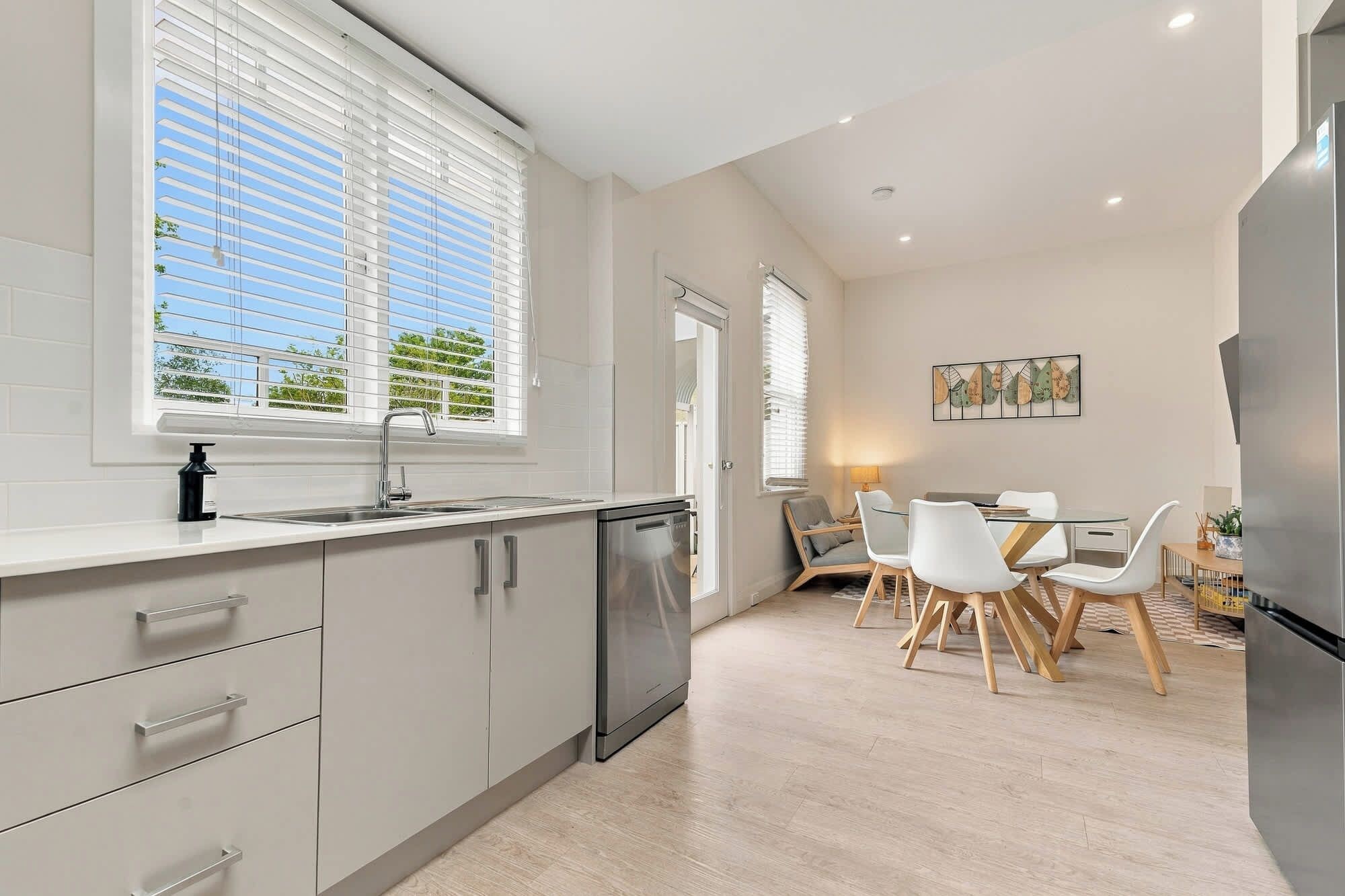 A modern kitchen with a built-in dishwasher, a dining area with a table and chairs, and a refrigerator.