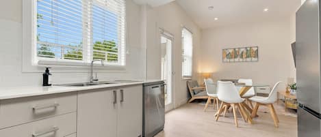 A modern kitchen with a built-in dishwasher, a dining area with a table and chairs, and a refrigerator.