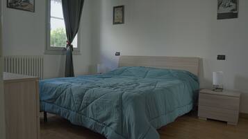 A bedroom with a bed, a nightstand, a dresser, and a window with curtains.