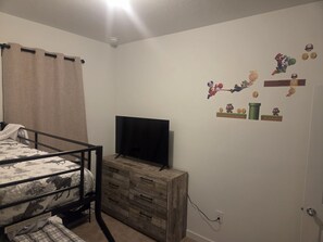 Une chambre avec un lit superposé, un téléviseur posé sur une commode en bois et des autocollants décoratifs sur les murs.