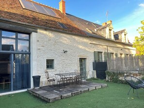 Uma casa com fachada de pedra, um pátio com mesa e cadeiras, e um quintal cercado.