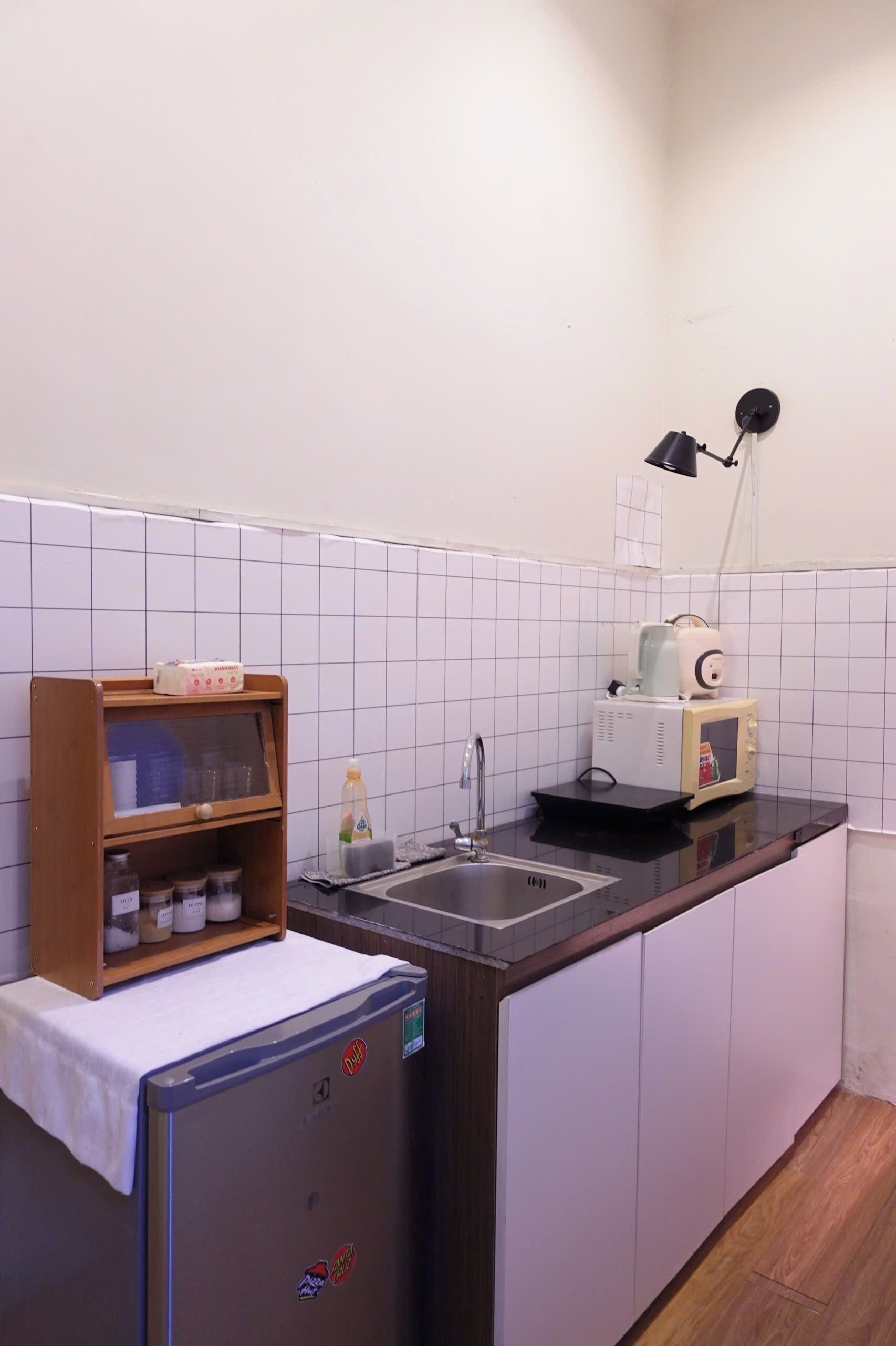 Une petite cuisine équipée d’un réfrigérateur, d’un four à micro-ondes, d’un évier et d’une étagère où sont rangés des bocaux.
