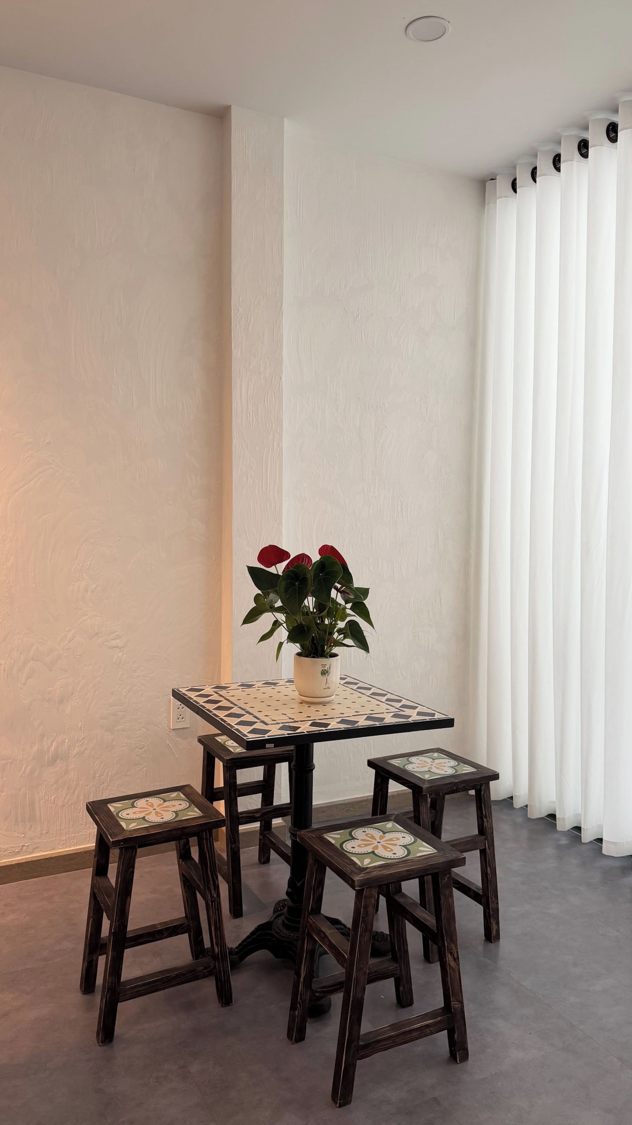 A dining area with a table and four chairs, a potted plant, and a window with curtains.