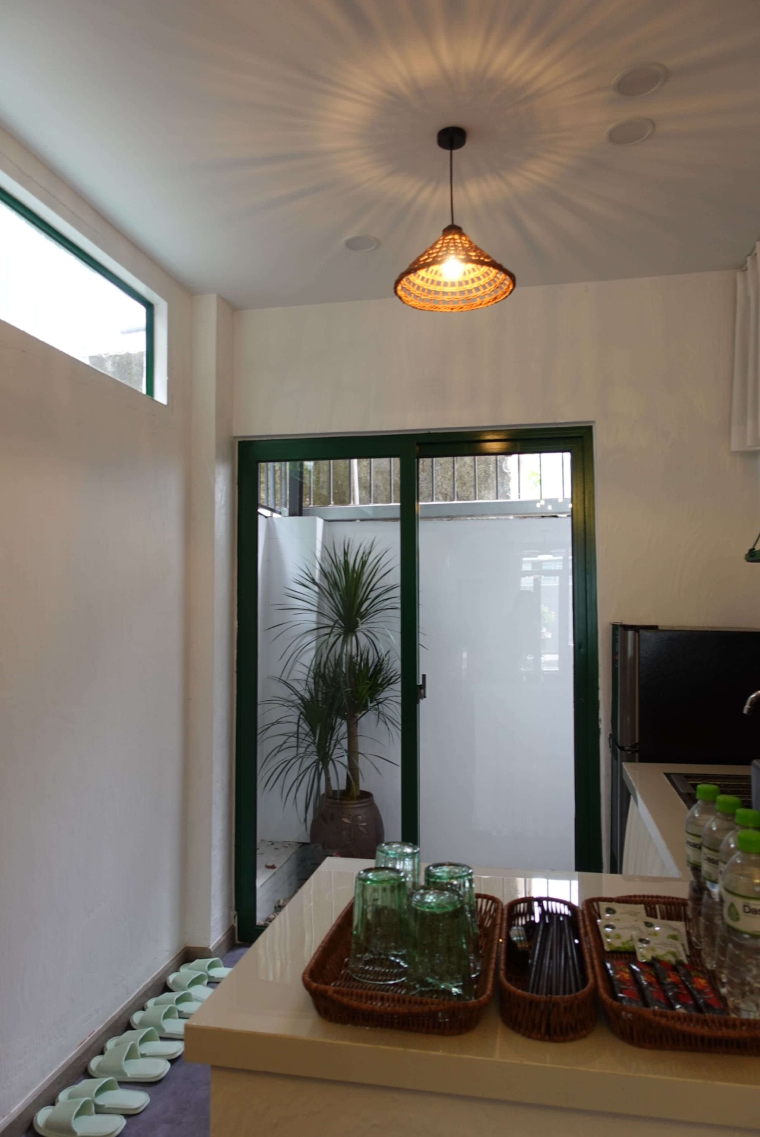 A kitchen with a hanging light fixture, a potted plant, and a counter with glass containers and bottles.