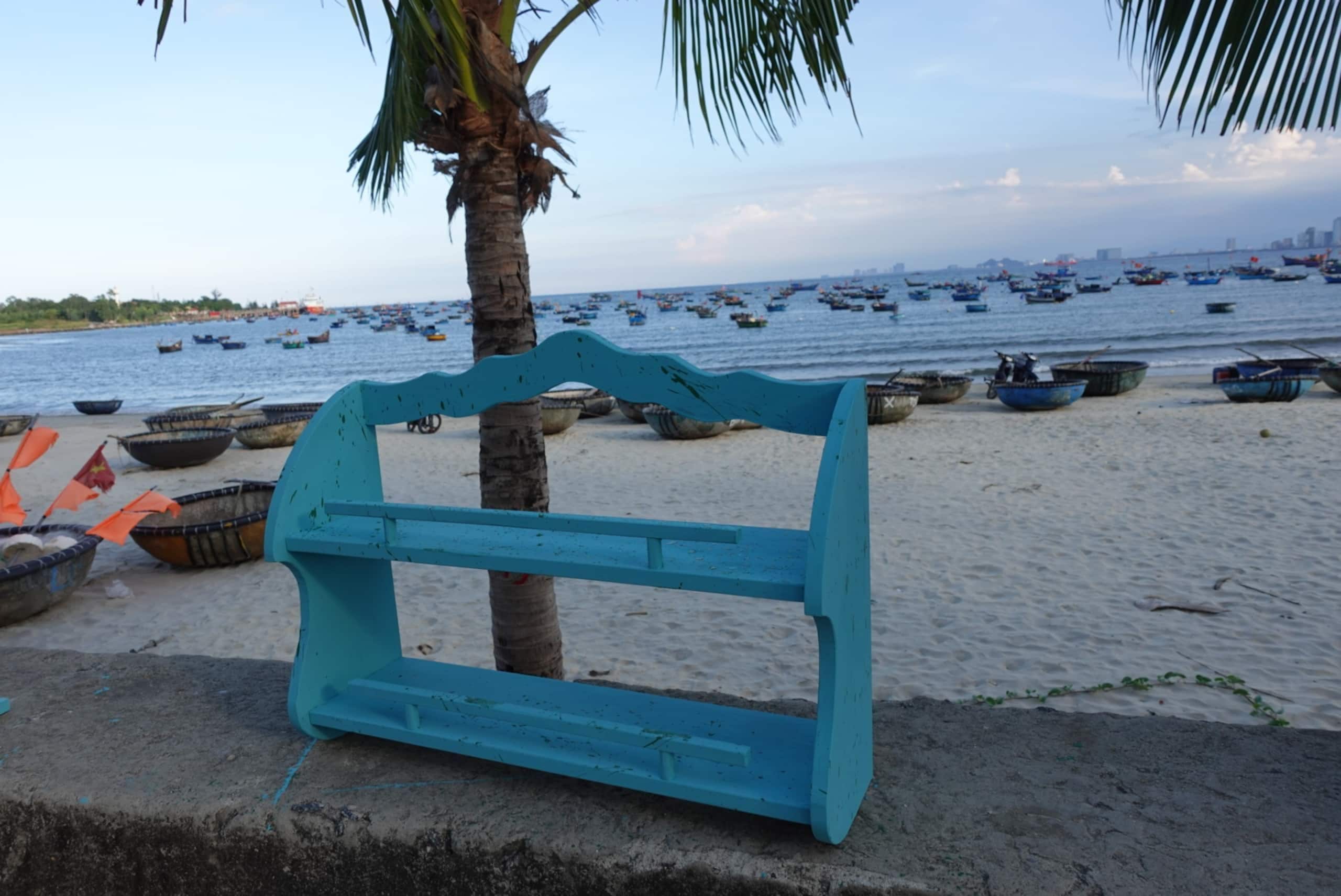 A beach with boats and a blue bench.