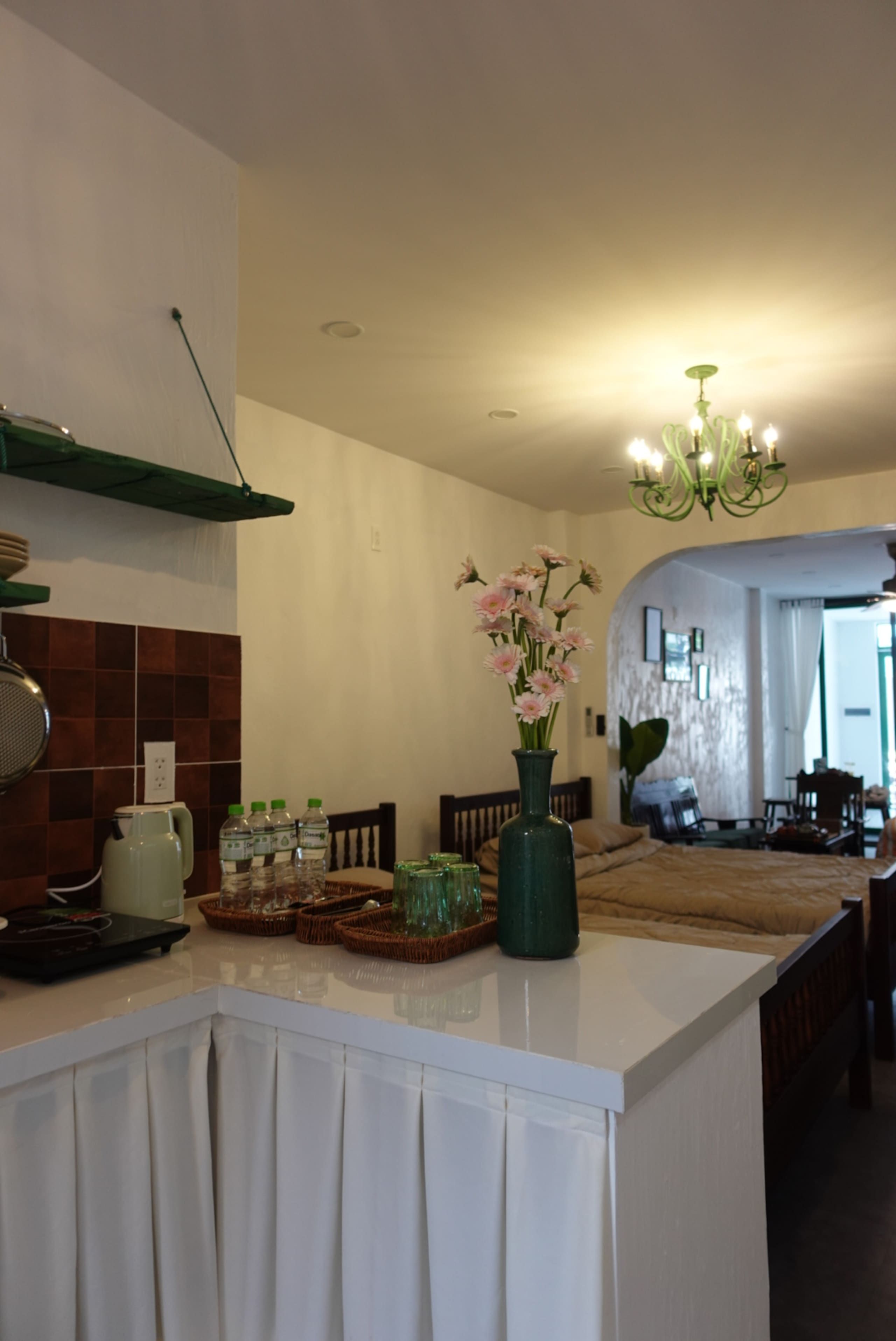 A kitchen with a white countertop, a green vase with flowers, and a chandelier.