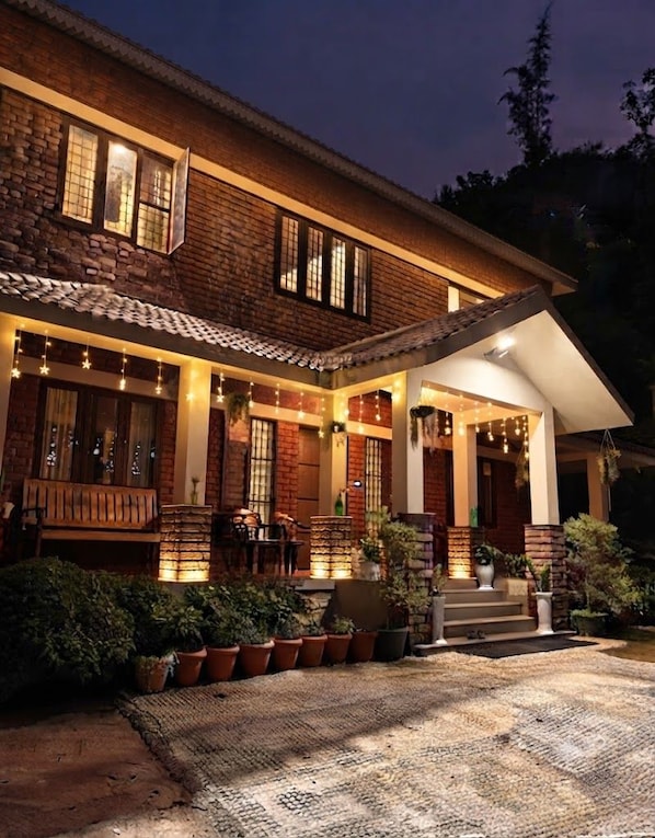 A brick house with a porch, outdoor seating, and potted plants.