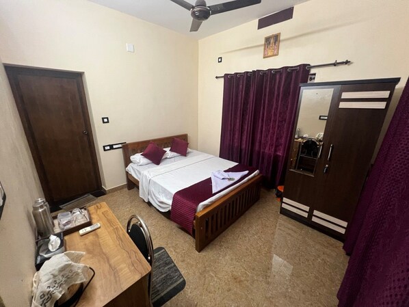 A bedroom with a bed, a wooden desk, a wardrobe, and a ceiling fan.