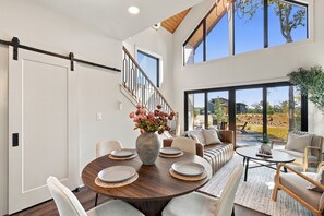 A spacious living area with a dining table, sofas, and a staircase leading to an upper level. - Views, Minigolf, Arcade, Sauna/Hot tub, New Aframe (Ellijay)