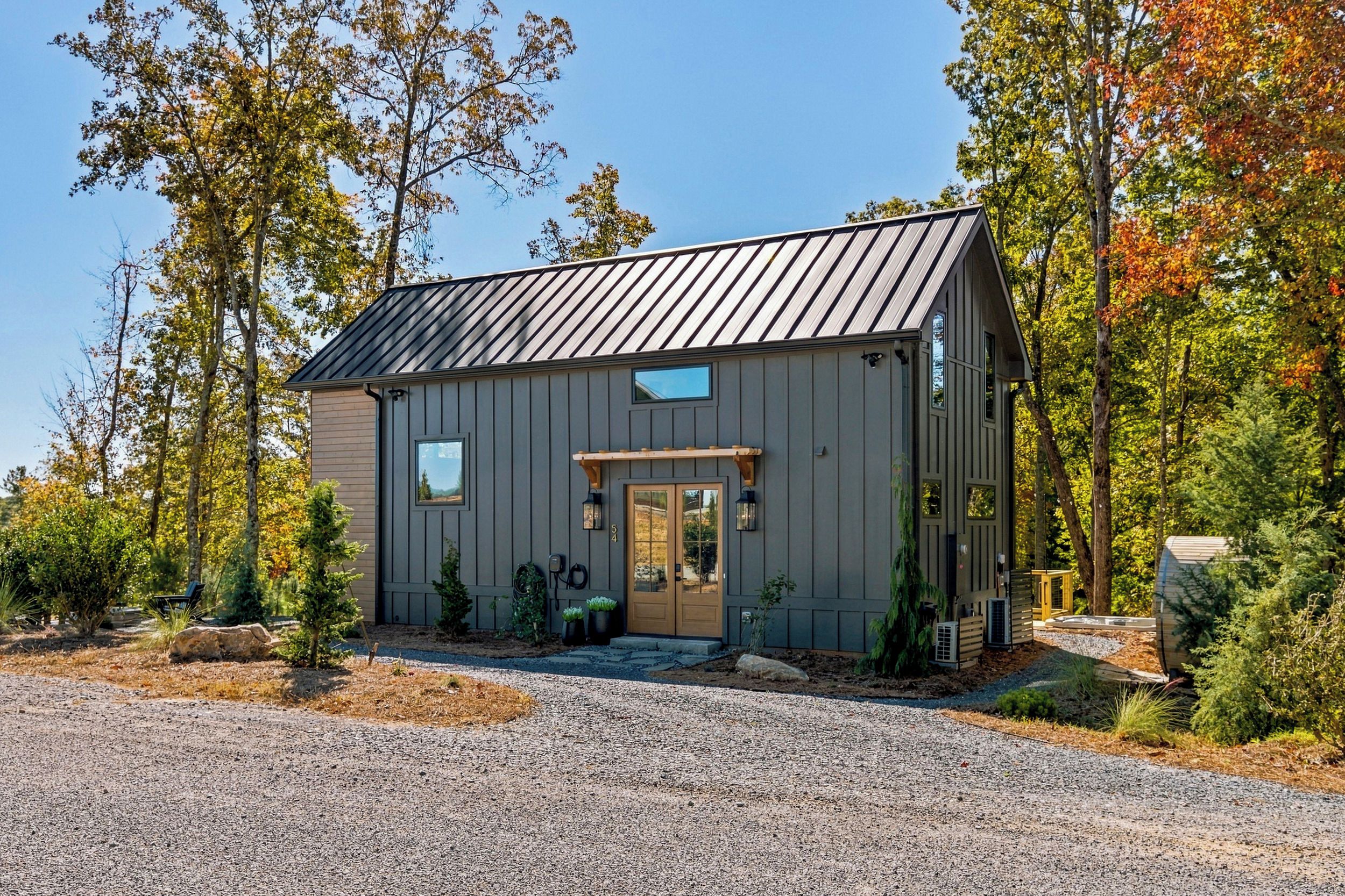 A modern cabin with a metal roof, a front porch, and a gravel driveway.