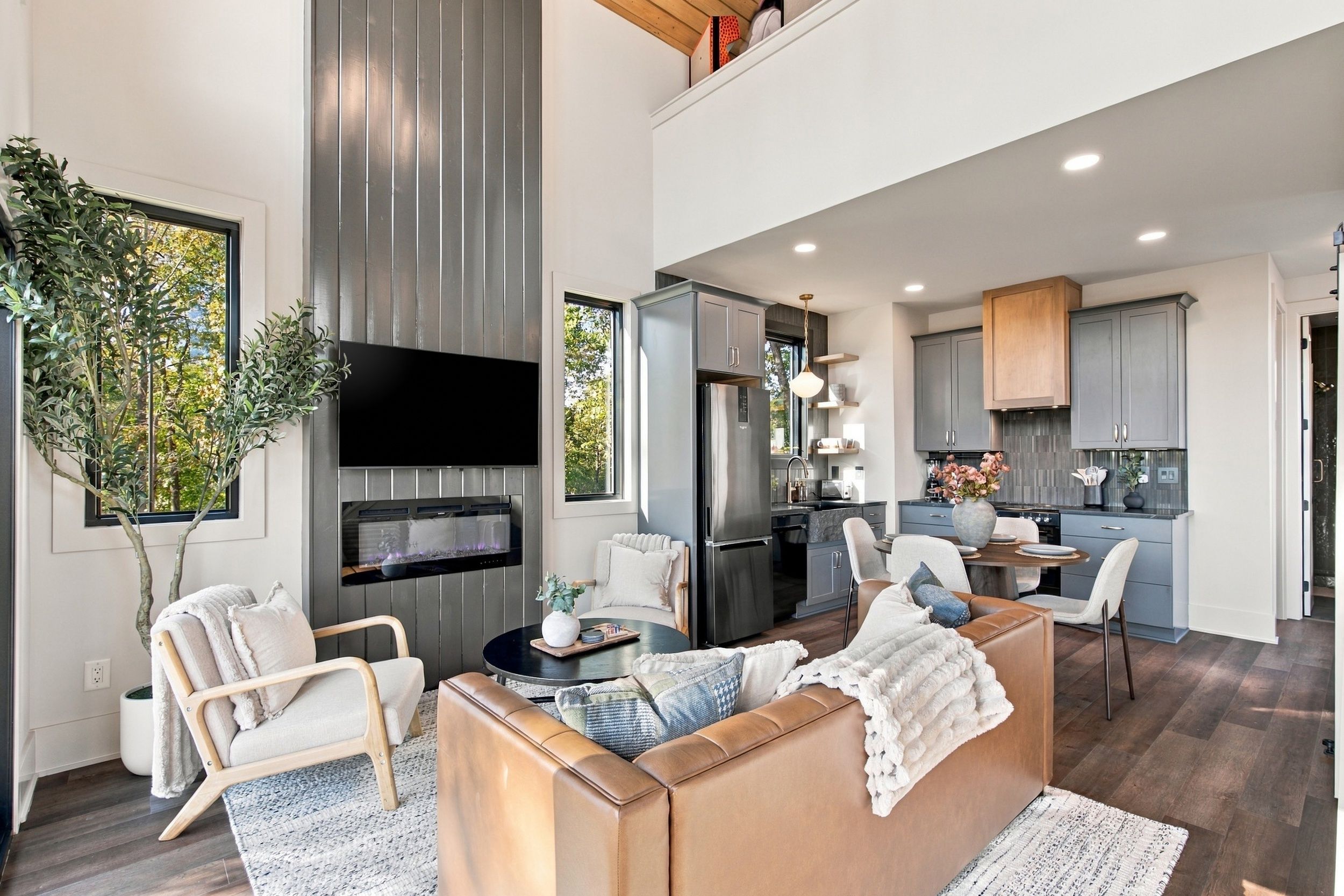 A modern living room with a fireplace, seating area, and a view of the kitchen.