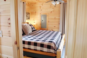 Habitación de cabaña de madera con una cama, un mesita de noche, una lámpara y una puerta.
